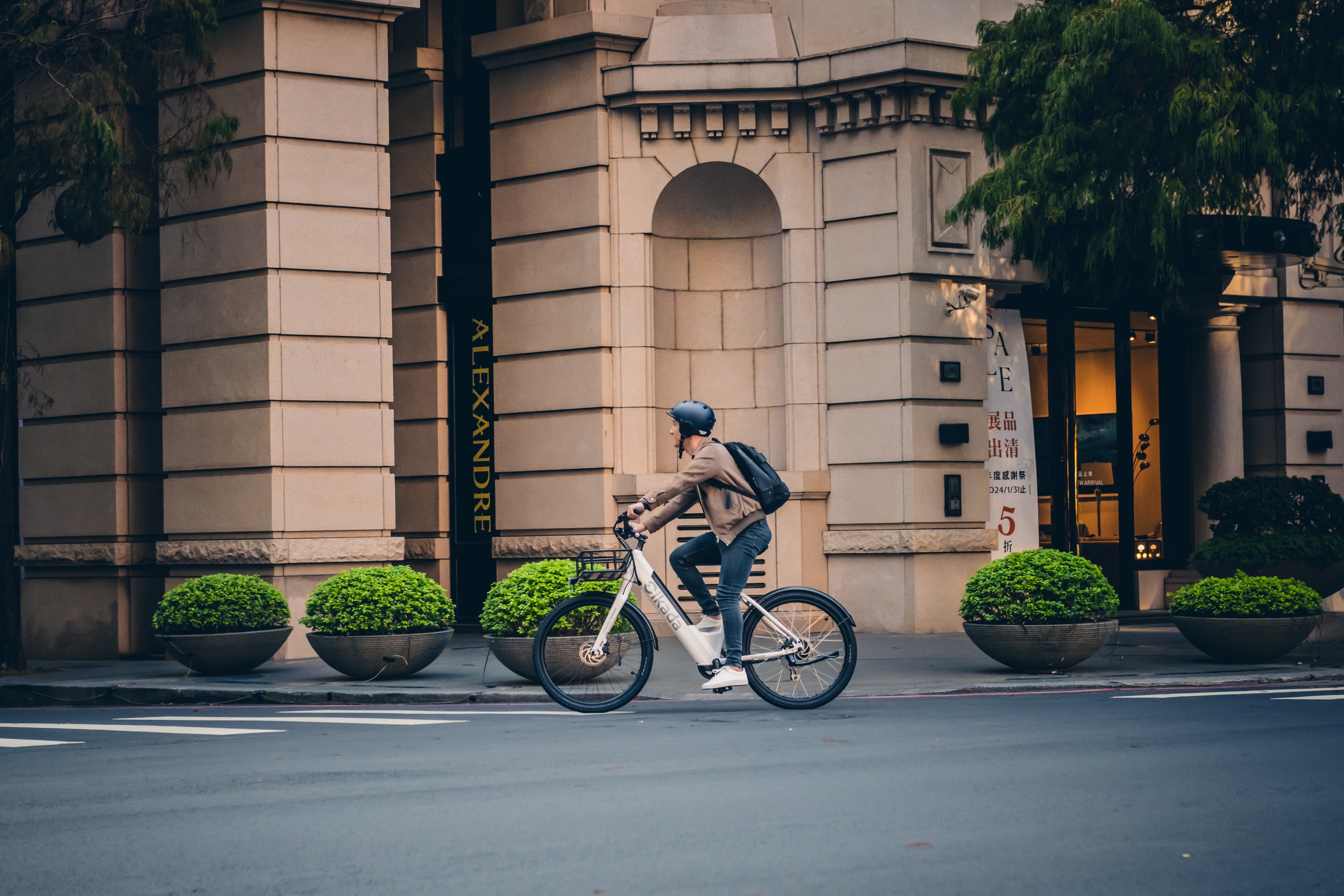 A man with helmet is riding through the city, in the background is fancy residential building.